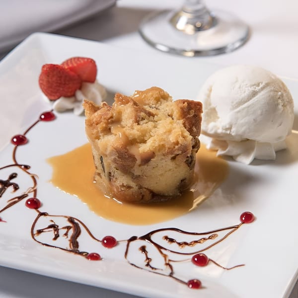 Bread pudding with caramel sauce, vanilla ice cream, whipped cream, strawberries, and chocolate drizzle.
