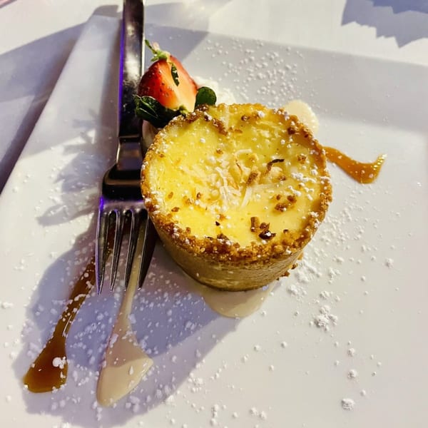 A lemon tart with a graham cracker crust, topped with powdered sugar, a strawberry, and mint.