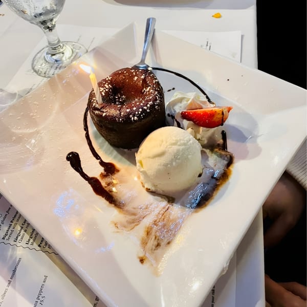Chocolate lava cake with a lit candle, vanilla ice cream, whipped cream, and a strawberry slice.