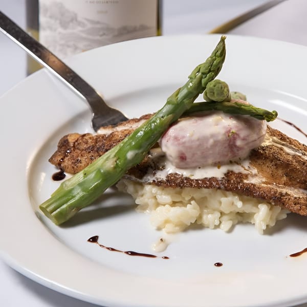 Pan-seared fish with asparagus, risotto, and a creamy sauce on a white plate.