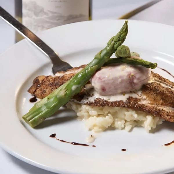 Pan-seared fish with risotto, asparagus, and a creamy sauce on a white plate.