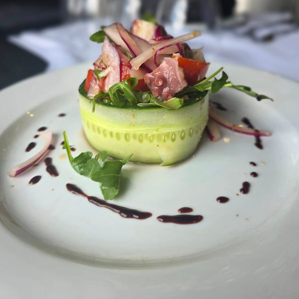 Octopus salad with red onions, tomatoes, and arugula, wrapped in cucumber on a white plate.